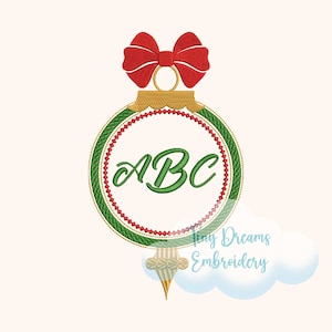 Puede incluir: Un adorno navideño verde y rojo con una parte superior dorada y un lazo rojo. El adorno tiene un círculo blanco en el centro con las letras "ABC" en verde.