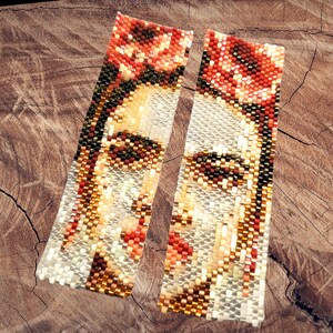 May include: A pair of long, beaded earrings with a colorful portrait of a woman. The earrings are made of small, colorful beads and feature a detailed design.