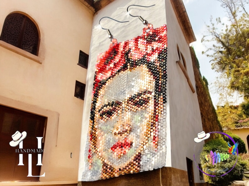 May include: A pair of handmade beaded earrings featuring a portrait of Frida Kahlo with red flowers in her hair. The earrings are hanging on a white wall.