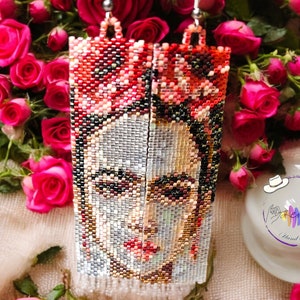 May include: A pair of long, beaded earrings featuring a colorful portrait of Frida Kahlo. The earrings are made with small, colorful beads and have a silver-toned metal hook.