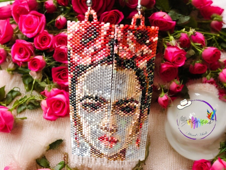 May include: A pair of long, beaded earrings featuring a colorful portrait of Frida Kahlo. The earrings are made with small, colorful beads and have a silver-toned metal hook.