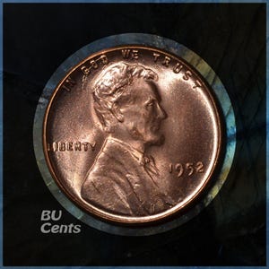 May include: A copper-colored 1952 Lincoln penny. The obverse side features a profile of Abraham Lincoln, the word "LIBERTY", and the year "1952". The coin is set against a dark, textured background with the text "BU Cents".
