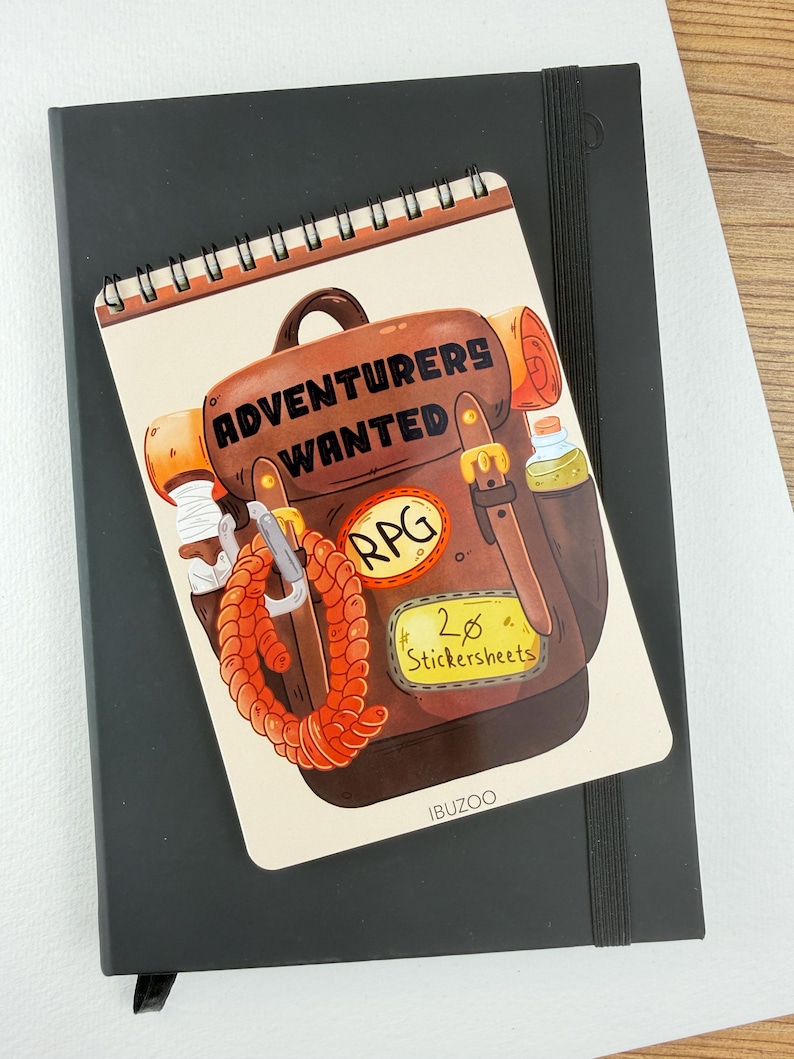 Op de afbeelding: Een spiraalgebonden notitieblok met een cartoonillustratie van een bruine rugzak met de tekst "ADVENTURERS WANTED" en "RPG". Het notitieblok ligt bovenop een zwart notitieboek. Het notitieblok heeft ook een stickervel label met "20 Stickersheets".