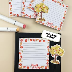 Könnte beinhalten: Ein Notizblock mit linierten Seiten und einem dekorativen Rand aus Kirschen, Eiswaffeln und Schleifen. Ein Aufkleber mit einem Baum und dem Text "Free maxi sticker" befindet sich neben dem Notizblock. Zwei weiße Marker mit rosa und orangefarbenen Spitzen sind ebenfalls sichtbar.