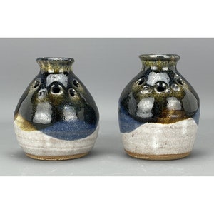 May include: Two small, round, ceramic vases with a blue, white and brown glaze. The vases have holes around the top for flowers or other decorative items.