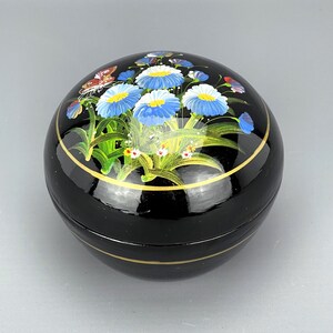 May include: Black round wooden box with a gold trim and a painted design of blue and white flowers and a butterfly.