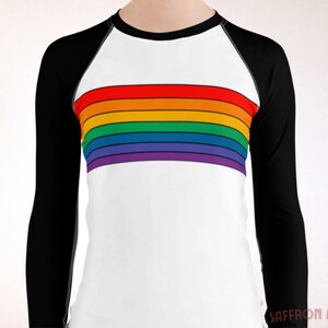 May include: A white long-sleeve shirt with black raglan sleeves and a rainbow stripe across the chest. The shirt has a crew neck.