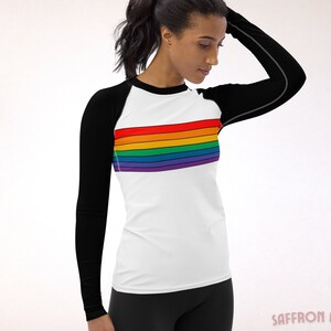 May include: A white long-sleeve shirt with black sleeves and a rainbow stripe across the chest. The shirt is made of a stretchy, athletic material.