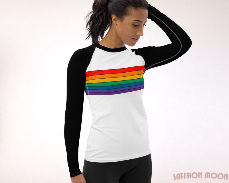 May include: A white long-sleeve shirt with black sleeves and a rainbow stripe across the chest. The shirt is made of a stretchy, athletic material.