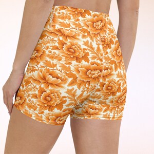 May include: Orange and white floral print athletic shorts. The shorts are made of a stretchy fabric and have a high waist.