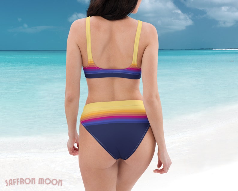 May include: A woman wearing a blue and yellow striped bikini with a high-waisted bottom. The bikini has a retro-inspired design with a rainbow stripe pattern.