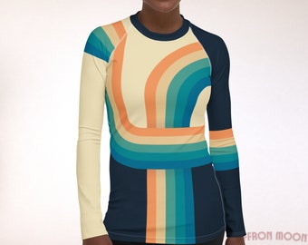 Puede incluir: Una camisa de manga larga con un diseño de inspiración retro que presenta un patrón de arcoíris colorido en tonos de azul, naranja y crema. La camisa tiene una base azul marino con un diseño de manga raglan.