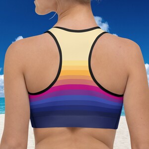 May include: A sports bra with a colorful striped pattern in shades of yellow, orange, pink, purple, and blue. The bra has a racerback style and black straps.