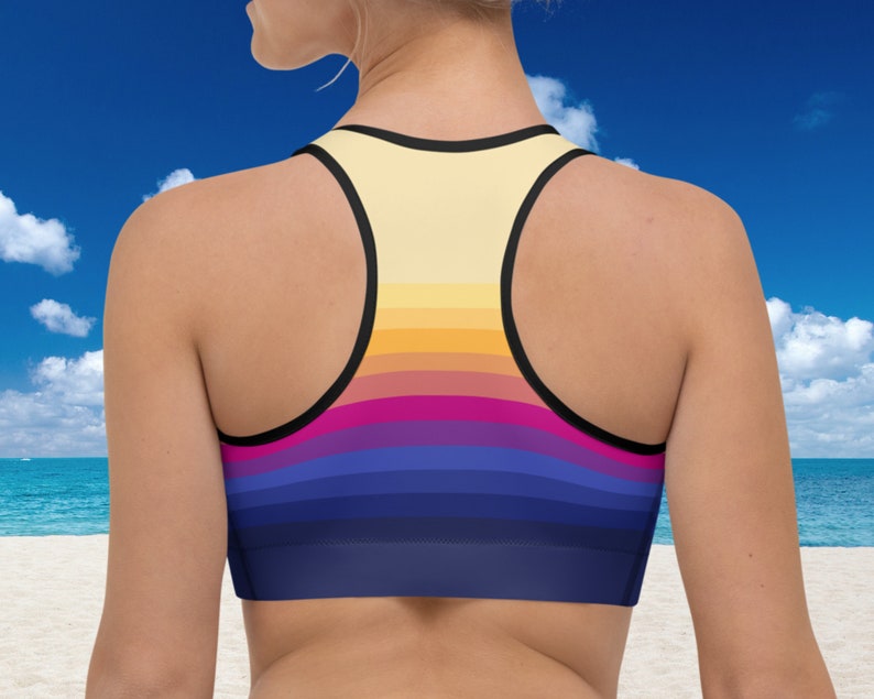 May include: A sports bra with a colorful striped pattern in shades of yellow, orange, pink, purple, and blue. The bra has a racerback style and black straps.