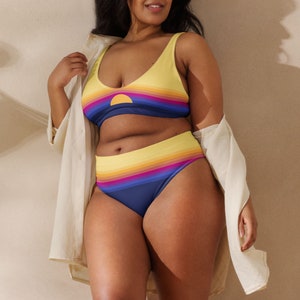 May include: A yellow and blue striped bikini with a sunset graphic. The top is a scoop neck style and the bottom is a high-waisted style.