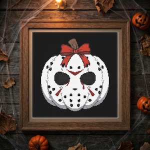 May include: A cross-stitch pattern framed in wood featuring a white pumpkin shaped like a hockey mask with black dots, a brown stem, and a large red bow on top, set against a solid black background within the square frame.