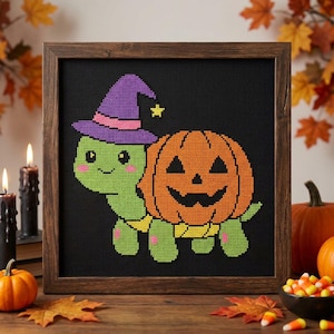 May include: A cross-stitch artwork in a dark wood frame featuring a light green turtle wearing a purple witch hat with a pink band and a small yellow star. The turtle has a large orange jack-o'-lantern pumpkin shell on its back.