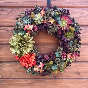 May include: A green, red, and pink succulent wreath with a variety of textures and colors. The wreath is hanging on a wooden door.