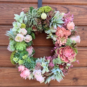 May include: A green and pink succulent wreath with pink roses hanging on a wooden door.