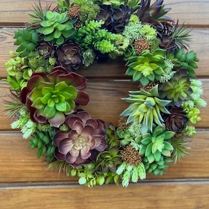 May include: A green and brown succulent wreath with a variety of different succulent plants. The wreath is hanging on a wooden door.