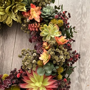May include: A green and red succulent wreath with a variety of succulents and greenery. The wreath is made of artificial succulents and is perfect for adding a touch of nature to your home decor.
