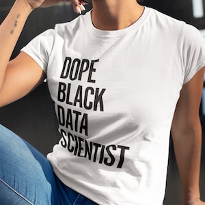 Könnte beinhalten: Weißes T-Shirt mit dem Text "DOPE BLACK DATA SCIENTIST" in Schwarz. Die Person auf dem Bild trägt eine Brille und eine blaue Jeans. Das Bild wurde im Freien aufgenommen.