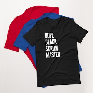 Puede incluir: Camiseta negra con texto blanco que dice "Dope Black Scrum Master". La camiseta se muestra doblada sobre una camiseta roja y una camiseta azul.