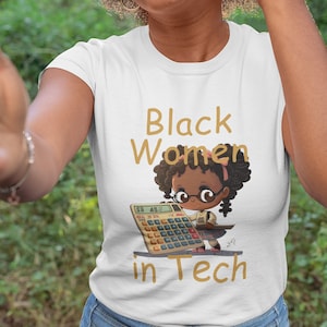 Puede incluir: Camiseta blanca con un gráfico dorado de una niña negra con gafas y sosteniendo una calculadora. El texto "Black Women in Tech" está impreso en dorado en la camiseta.