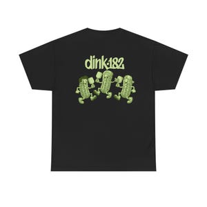 May include: Black t-shirt with a green graphic of three pickle characters holding paddles, with the text "dink182" above them. The pickles are depicted with different hats and expressions. The shirt is made of a soft material.