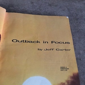 May include: A book cover with a yellow background and a sunset scene. The title is "Outback in Focus" by Jeff Carter. The book is published by Angus & Robertson (UK) Ltd.