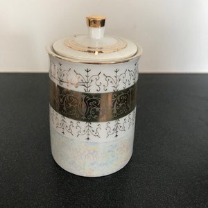 May include: White porcelain sugar jar with a gold lid and gold trim. The jar has a black and gold floral design.