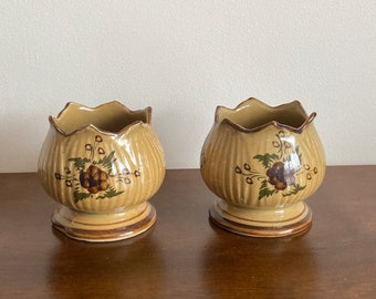 May include: Two small, brown ceramic flower pots with a floral design. The pots have a scalloped rim and a flared base.