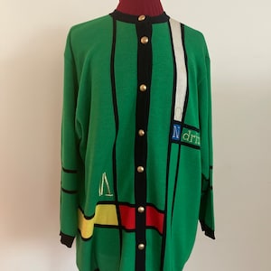 May include: Green cardigan with a geometric design featuring black, yellow, red, and white accents. The sweater has gold buttons and the word "Ndrin" embroidered on the front. The collar is a dark red.