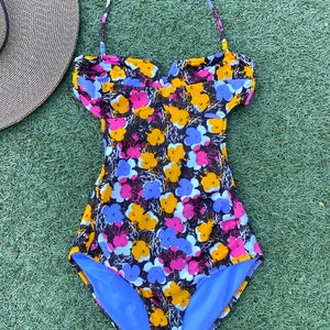 May include: A black swimsuit with a floral print in shades of yellow, pink, and blue. The swimsuit has a halter neck strap and a sweetheart neckline.