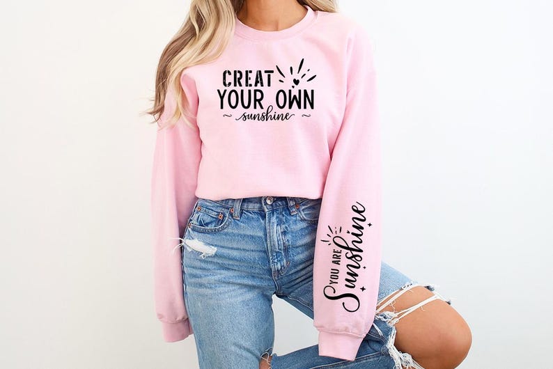 Pode incluir: Camisola cor-de-rosa com o texto "Crie o seu pr&oacute;prio sol" na frente e "Voc&ecirc; &eacute; o sol" numa manga.