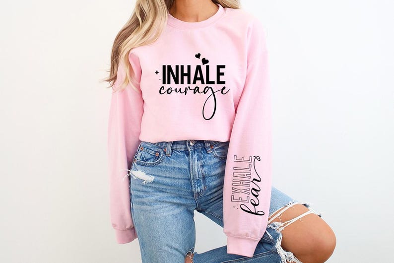 Pode incluir: Camisola cor-de-rosa com o texto "INHALE courage" na frente e "EXHALE fear" na manga.