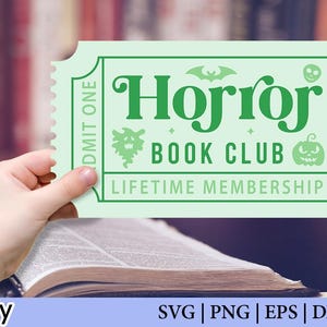 May include: A pale green ticket with the words "Horror Book Club Lifetime Membership" in green. The ticket features a bat, skull, and pumpkin graphic. The ticket is held over an open book.