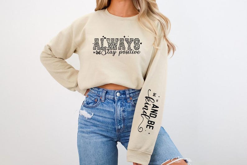 Pode incluir: Uma camisa de moletom bege com o texto "ALWAYS Stay positive" na frente e "AND BE kind." na manga.