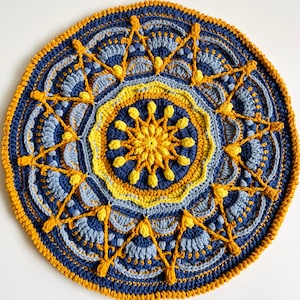 May include: A crocheted mandala with a blue and yellow color scheme. The center of the mandala features a yellow flower with blue petals. The mandala is surrounded by a border of blue and yellow crocheted stitches.
