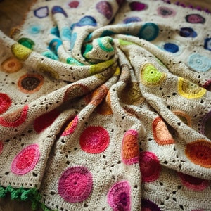 May include: A crocheted blanket with a beige background and colorful circular patterns. The blanket is made with a variety of colors, including red, orange, yellow, green, blue, and purple.