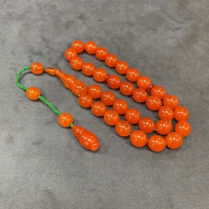 May include: A string of orange prayer beads with a green tassel. The beads are made of a smooth, translucent material.