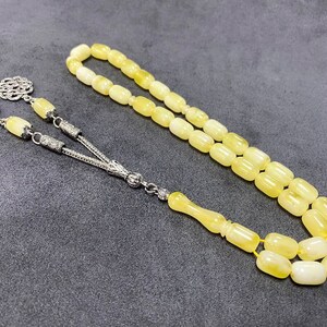 Puede incluir: Un collar de cuentas de oraci&oacute;n de &aacute;mbar amarillo con detalles plateados. Las cuentas son de forma ovalada y el collar tiene un borla.