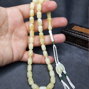 May include: A white and yellow prayer beads necklace with a white tassel. The beads are oval shaped and have a smooth, polished finish.