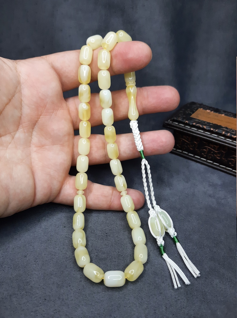 May include: A white and yellow prayer beads necklace with a white tassel. The beads are oval shaped and have a smooth, polished finish.