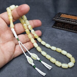 May include: A white and yellow prayer beads with a green tassel. The beads are strung on a white cord and are held in a hand.