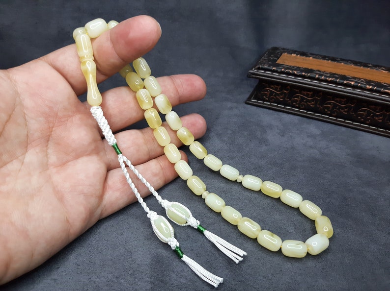 May include: A white and yellow prayer beads with a green tassel. The beads are strung on a white cord and are held in a hand.
