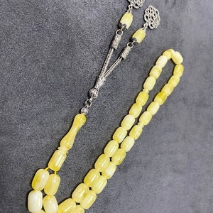 Puede incluir: Un collar de cuentas de oraci&oacute;n de &aacute;mbar amarillo con detalles plateados. Las cuentas son de forma ovalada y el collar tiene un borla.