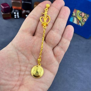 Peut inclure: Boucle d'oreille dorée avec un design détaillé. La boucle d'oreille comporte une chaîne avec un pendentif circulaire en bas. Le pendentif présente un motif d'aigle. Le haut de la boucle d'oreille a un élément décoratif avec une figure.