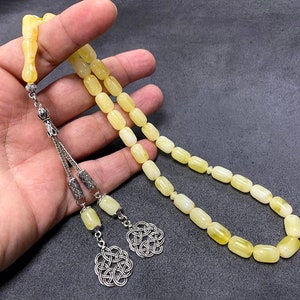 Puede incluir: Un collar de cuentas de oraci&oacute;n de &aacute;mbar amarillo con borlas y cierre de plata. Las cuentas son de forma ovalada y tienen un acabado liso y pulido.