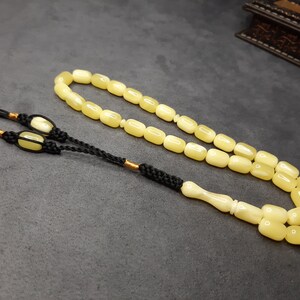 May include: A yellow amber prayer beads necklace with a black tassel and a white bone handle.